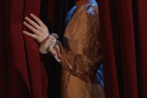 Woman's hand pulls back a stage curtain at a theater