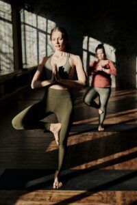 Two women holding tree pose in a yoga studio