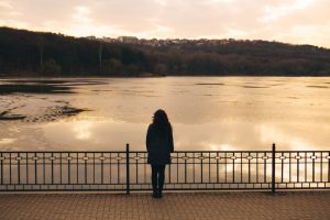 Woman standing on a bridge looking out to an ice covered winter lake