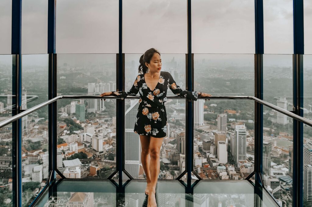 A high-achieving woman stands in a glass elevator overlooking the city struggling to feel worthy of her success. Therapy for Women in Manhattan, NY can help overcome these feelings of unworthiness.