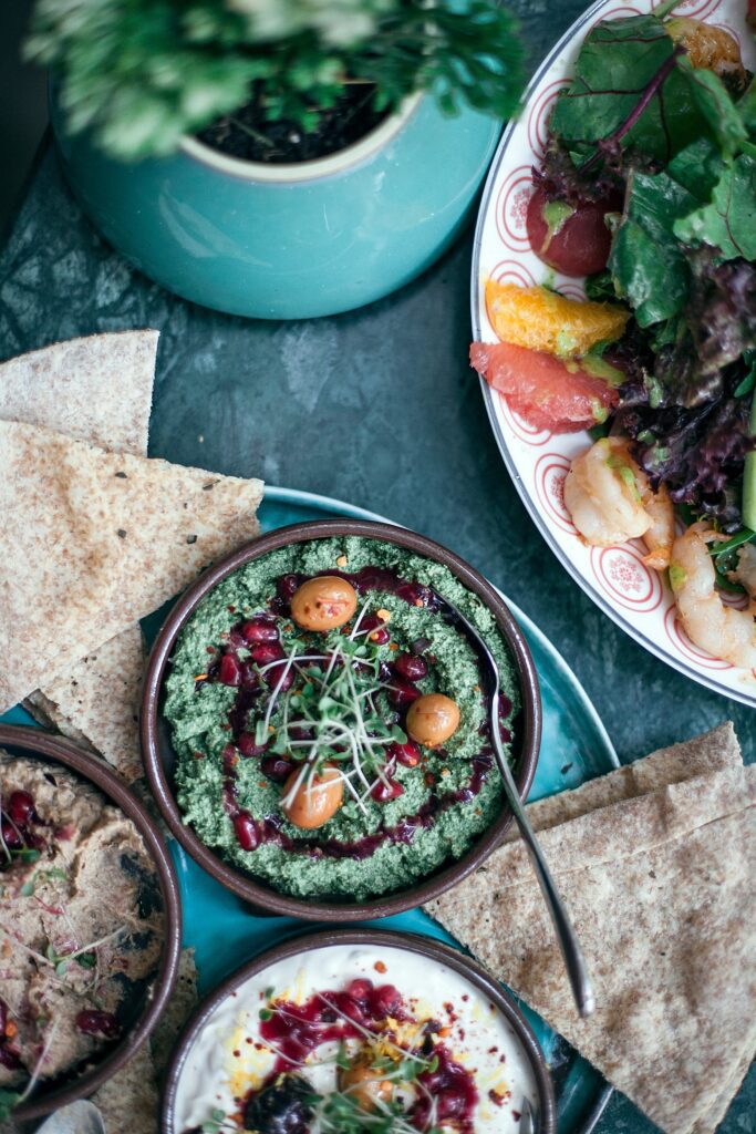 Humus and a salad on a blue table representing the positive impact healthy food can have on self-care. Learn more about self-care in Anxiety Therapy for Women in Manhattan, NY.