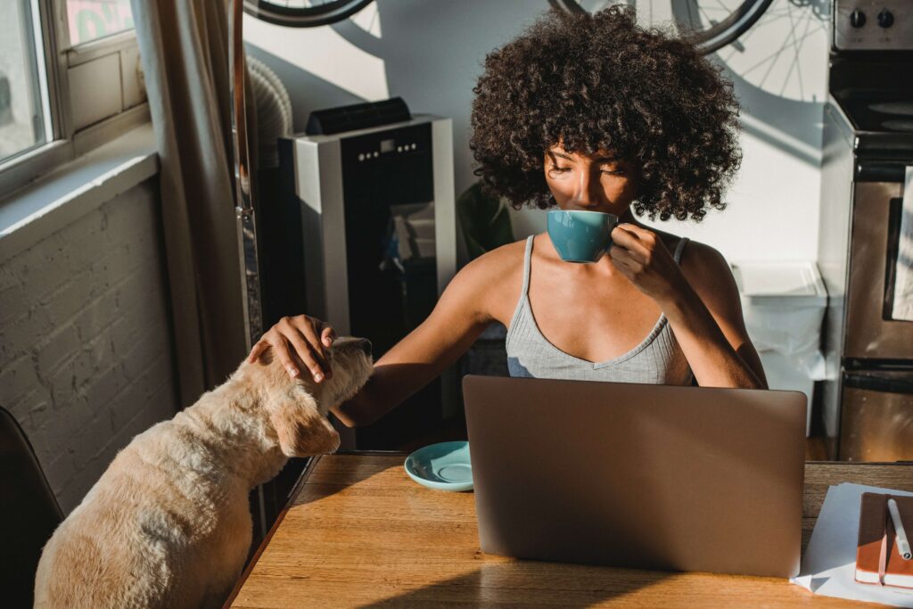 A woman drinks coffee and looks at her laptop while petting her dog representing someone who is discovering work life balance with the help of Anxiety Therapy for Women in Manhattan, NY.