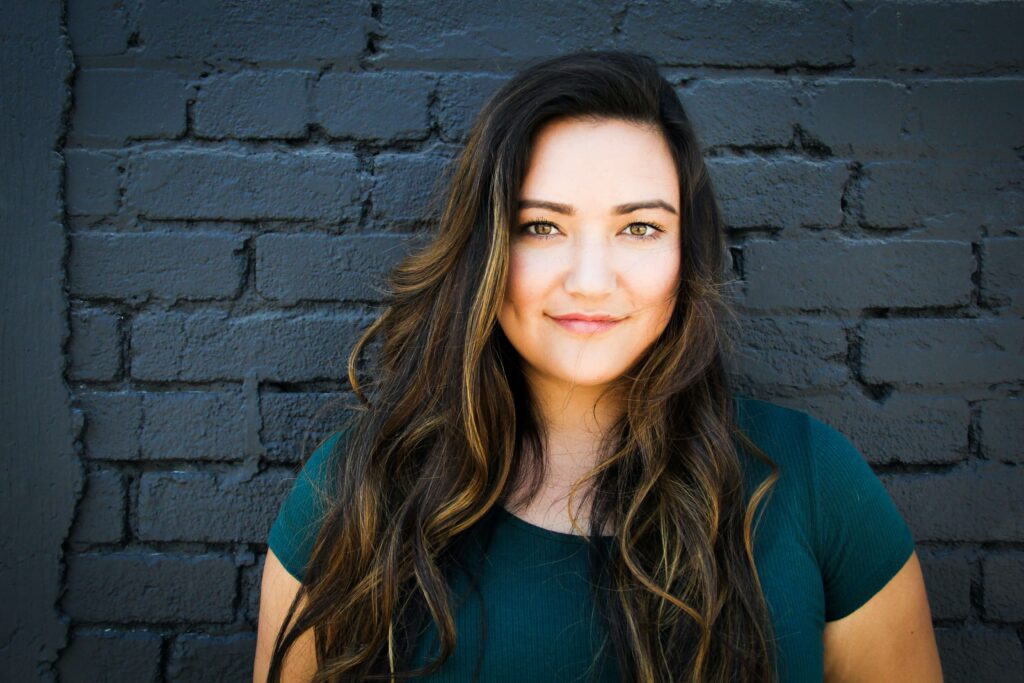 A woman stands against a blue wall. Don't let expectations overwhelm and control your life. Therapy for Women is a great resource for support. 