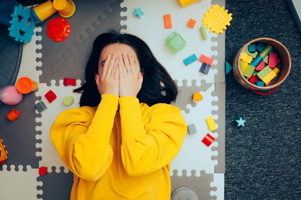 A mother lies on a playmat on the floor with her hands over her face, overwhelmed by parenting a neurodiverse child in NYC. Therapy for Special Needs Parenting can help.