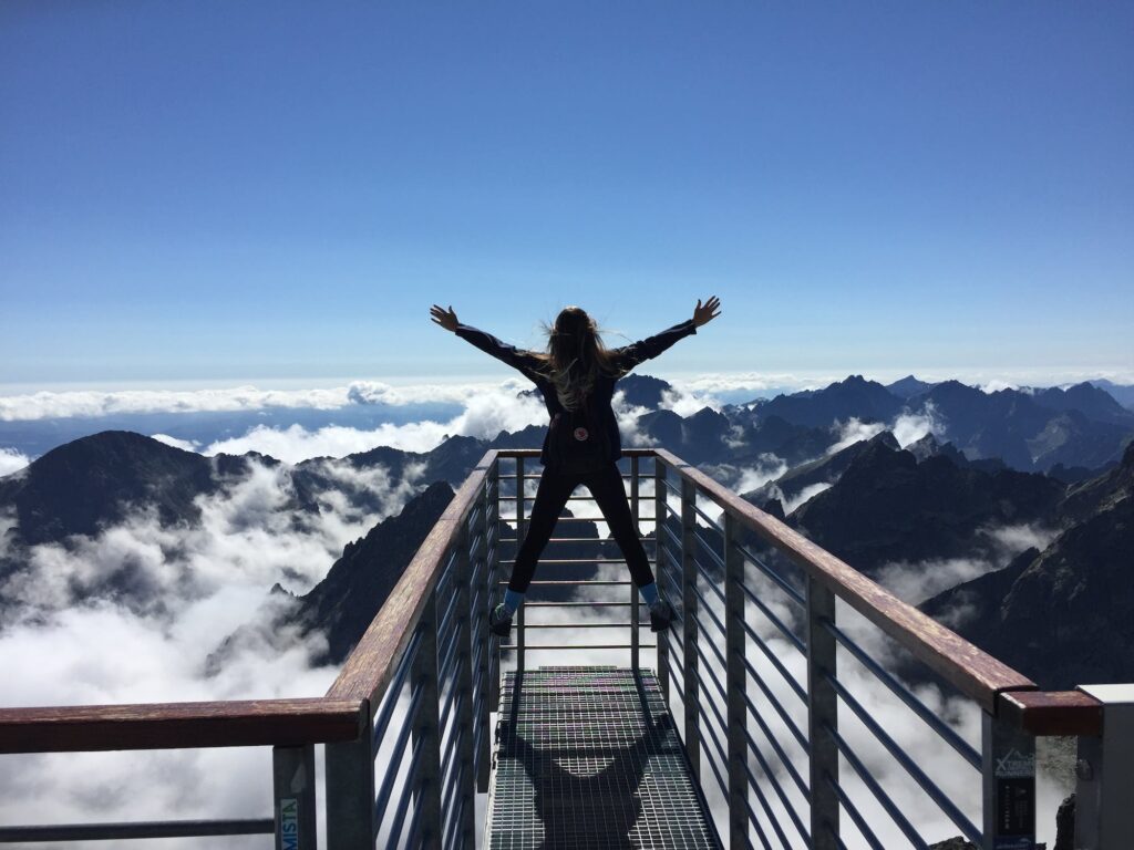 A person on top of a mountain with their hands up the air.