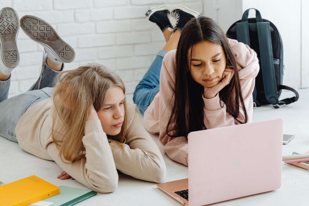 Two girls work on their laptops preparing for the transition to high school. Therapy for Teens in NYC can help navigate the ups and downs of starting high school. 