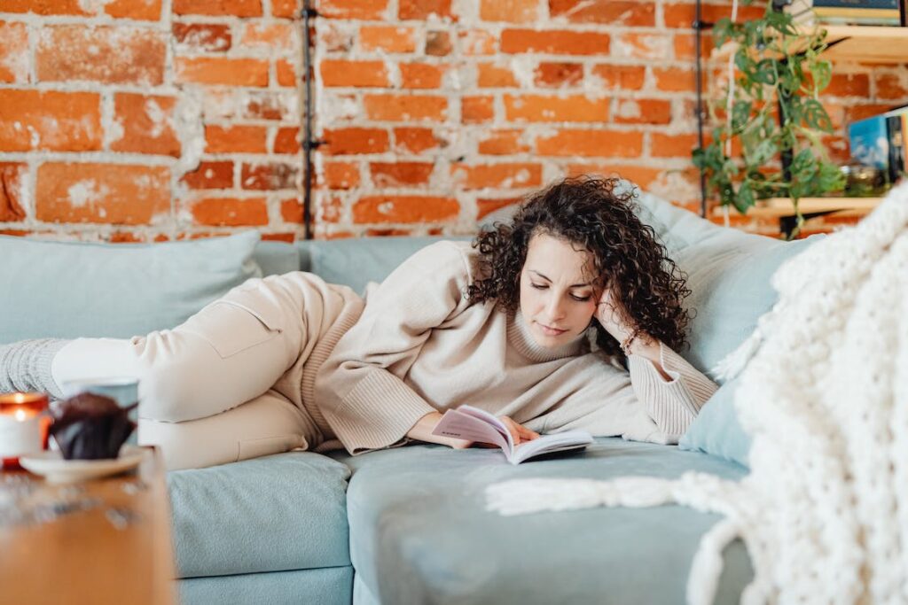 Relaxation amidst daily hustle: A woman finds solace, reading on a couch, illustrating mindful downtime in a bustling world.