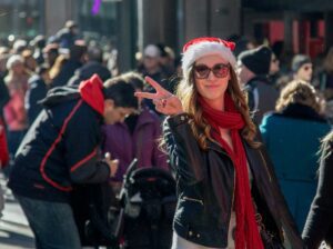 Woman in a Santa hat, standing amidst a crowd, giving the peace symbol during the festive season.